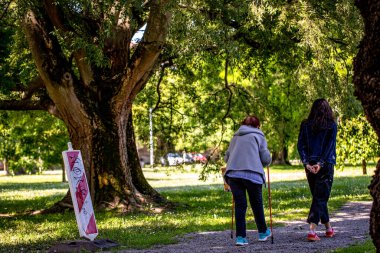 İki kadın yeşil bir parkta yürüyor, ağaçlarla çevrili.. 