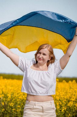 Kolza tohumu tarlasında özgürlüğü kutlayan beyaz kadın Ukrayna bayrağıyla poz veriyor.  