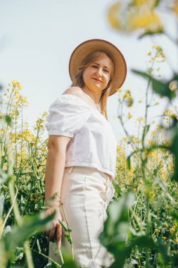 Huzurlu kırsal bölge, ilkbaharda altın bir kolza tohumu tarlasının tadını çıkaran zarif bir kadını çevreledi..