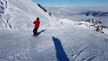 Snowboardcu Alplerin tozlu yamaçlarının tadını çıkarıyor.