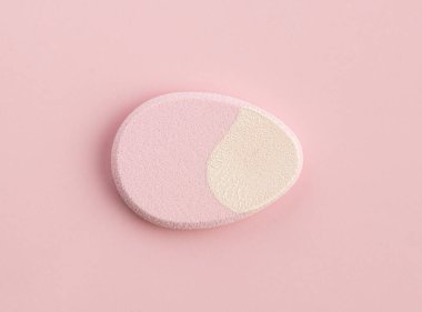 Pembe arka planda yumurta şeklinde kozmetik sünger. Üst görünüm