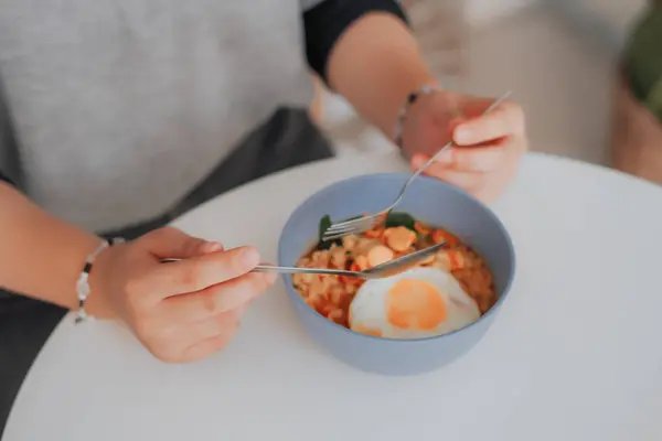 Kadının elinde kaşık ve çatalla pirinç lapası kasesi var.