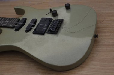 Close up photograph of electric guitar with broken guitar strings on a wooden bench.