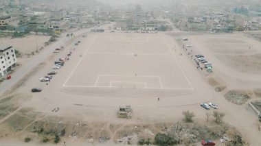 Güneşli ve sisli bir günde etrafı tepelerle çevrili fakir ve kalabalık bir köyde birkaç kişinin oynadığı büyük bir toprak futbol sahası.