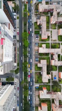 Ağaçlarla dolu ve binalarla çevrili bir kavşakta kaldırımda yürüyen araba ve yaya trafiği yukarıdan insansız hava aracı ile görülüyor.