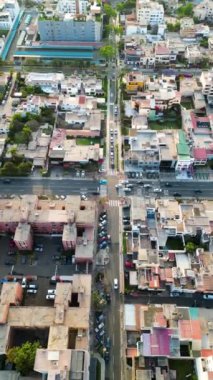  Hafif araba trafiği ve ağaçlarla çevrili ve gökyüzünden insansız hava aracıyla görülen binalarla çevrili kavşakta yürüyen insanlar.