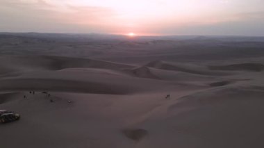 Gün batımında insansız hava aracı bir grup insanı ve çöl arabalarını yakalıyor.