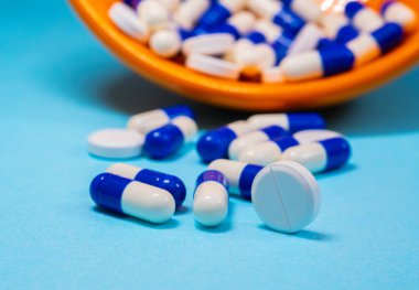 İlaç dolu turuncu bir konteynırın önüne dizilmiş beyaz ve mavi kapsüller..