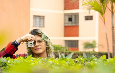 Şehir ortamında yeşil saçlı, klasik fotoğraf makinesiyle fotoğraf çeken bir genç..