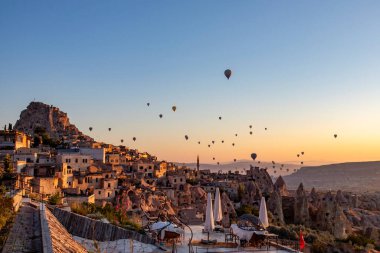 Arka planda görkemli dağların yükseldiği göz kamaştırıcı bir vadi manzarası, nefes kesici bir doğal manzara, şafak vakti sıcak hava balonları, Cappadocia 'daki volkanik tufa dağlarının ve mağara evlerinin zeminine karşı..