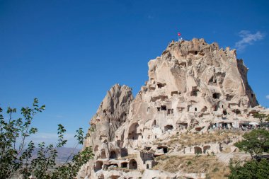 Önemli ve etkileyici bir kaya oluşumu, üzerinde gururla dalgalanan bir bayrak, bir yolculuğu ya da macerayı sembolize eder. İçinde mağara geçitleri olan bir kaya şatosu.