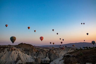 A stunning view of a picturesque valley with majestic mountains rising in the background, creating a breathtaking natural landscape, hot air balloons at dawn against the backdrop of volcanic tufa clipart