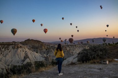 Arka planda görkemli dağların yükseldiği büyüleyici bir vadi manzarası, nefes kesen doğal bir manzara, şafak vakti volkanik tufa zeminine karşı sıcak hava balonları yaratıyor.