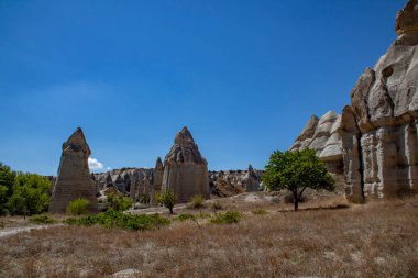 Derin mavi gökyüzü ve aile, içinde hâlâ mağara evleri olan Tuff 'tan yapılmış mantar şekilli kayalarda yürüyor. Aşk Vadisi 'ndeki Kapadokya seyahatinin yaz havası
