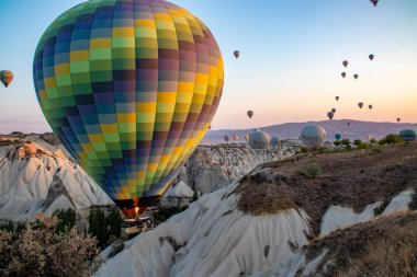 Arka planda görkemli dağların yükseldiği büyüleyici bir vadi manzarası, nefes kesen doğal bir manzara, şafak vakti volkanik tufa zeminine karşı sıcak hava balonları yaratıyor.