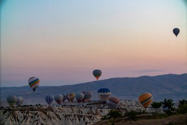 A stunning view of a picturesque valley with majestic mountains rising in the background, creating a breathtaking natural landscape, hot air balloons at dawn against the backdrop of volcanic tufa clipart