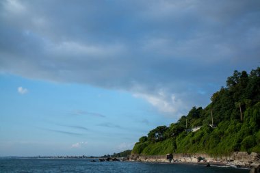 Görkemli bir şekilde suların sakin bir gövdesine bakan muhteşem bir uçurum, yemyeşil ağaçlar ve çevresindeki yapraklarla.