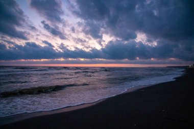 Bu, gün batımında güzel bir plajı gösteren bulanık bir fotoğraf. Bulutlu bir gökyüzü sahnenin sakin atmosferine katkı sağlıyor.