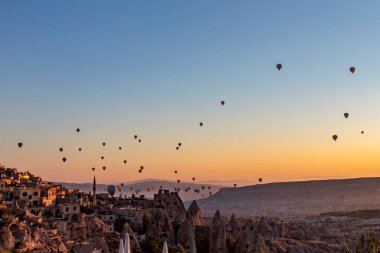 Arka planda görkemli dağların yükseldiği büyüleyici bir vadi manzarası, nefes kesen doğal bir manzara, şafak vakti volkanik tufa zeminine karşı sıcak hava balonları yaratıyor.