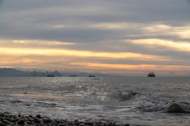 Güneş, dingin bir su kütlesinin üzerinde görkemli bir şekilde batarken, uzaklarda huzur içinde yüzen tekneler görülebilir, resim gibi bir manzara yaratabilir.