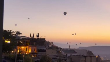 Cappadocia 'nın pitoresk bir kasabasında canlı bir günbatımına doğru sürüklenen renkli sıcak hava balonlarının çarpıcı manzarası.