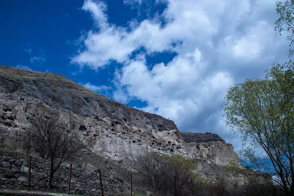 Nefes kesen bir dağ heybetli bir mavi gökyüzüne karşı duruyor. Kabarık bulutlar yavaşça arkasında sürükleniyor. Antik mağara şehri Vardzia.