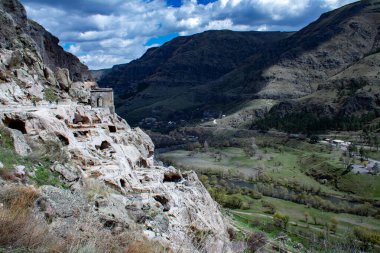 Nefes kesen bir dağ heybetli bir mavi gökyüzüne karşı duruyor. Kabarık bulutlar yavaşça arkasında sürükleniyor. Antik mağara şehri Vardzia.