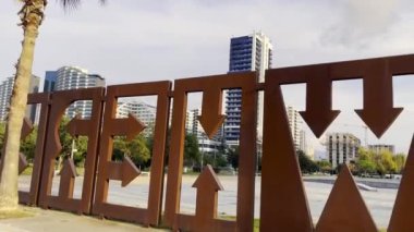 Canlı bir şehir sahnesinde modern binalar, yemyeşil alanlar ve yenilikçi sanatsal çitler yer alıyor.