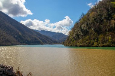 Parlak mavi gökyüzünün altındaki görkemli tepelerden zarif bir şekilde akan sakin bir nehri olan nefes kesici bir manzara.