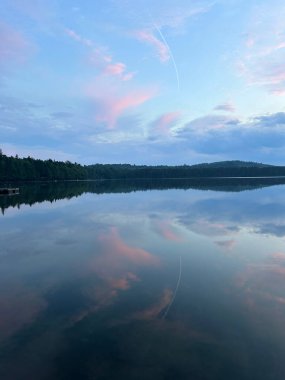 Pamuk helva bulutları, huzurlu bir göletin üzerinde süzülür ve durgun sulara ayna görüntüsü olarak yansıtılır.