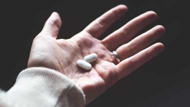 Bir el beyaz hap haplarını tutuyor. Minimalist, yakın plan.