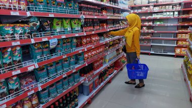 Pinrang-Makassar, Endonezya. 28 Ekim 2024: Bir süpermarkette mavi sepet taşıyan Asyalı kadın soslara ve tatlı soya sosuna bakıyor ve onları seçiyor.