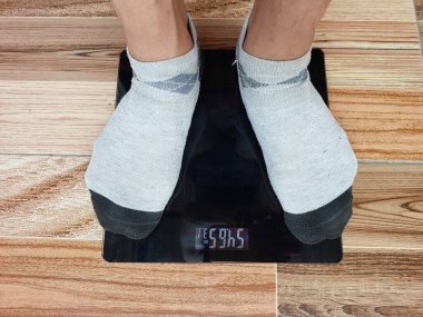 Erkek ayakları, kiloları ve ahşap zemindeki dambılları kontrol etmek için dijital terazide duran çoraplar giyer..