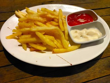 Yanında iki sos olan bir tabak patates kızartması, yani ketçap ve mayonez. Patates kızartması beyaz bir tabakta servis edilir..