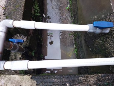 Suda ya da drenaj alanında mavi valfli iki beyaz PVC boru..