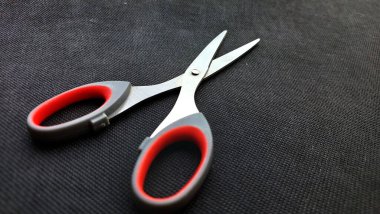 Siyah desenli bir yüzey üzerinde kırmızı ve gri saplı makas. Bu makasla ortada bir cıvata ile bağlanmış iki keskin bıçak var. Pratik ve zarif. Siyah arkaplan ile