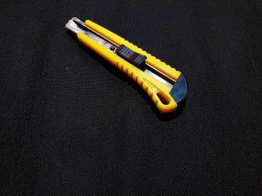 A cutter knife with a yellow plastic handle and a black tip, and a slightly visible metal blade. This tool is used for cutting paper, cardboard, or other thin materials.