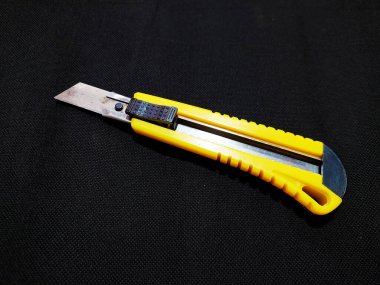 A cutter knife with a yellow plastic handle and a black tip, and a slightly visible metal blade. This tool is used for cutting paper, cardboard, or other thin materials.