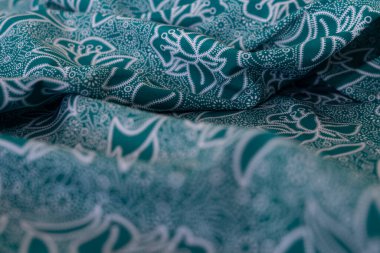 Bir desenli yeşil kumaş parçası. Kumaş katlanmış ve parlak bir görünüme sahip. Kumaş sentetik bir malzemeden yapılmıştır. Sancak, arkaplan veya 3B haritalama dokusu için arka plan