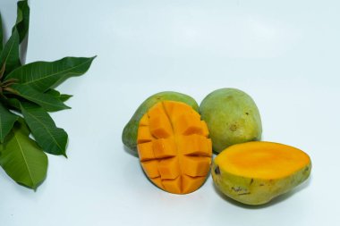 Beyaz arka planda yapraklı mango dilimleri ve yeşil mangolar.