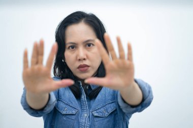 Mavi kot gömlekli bir kadın, iki eli havada ve yüzünün önünde çapraz yapmış. Avuç içleri açık, beyaz arka planda duran koruyucu bir jest, reddetme ya da dur işareti izlenimi veriyor.