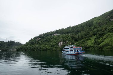 Ziyaretçiler, Toba Gölü, Simalungun, Kuzey Sumatra, Endonezya 'daki asılı taş turizm merkezine gitmek için motorlu tekne kullanıyorlar.