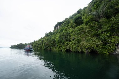 Ziyaretçiler, Toba Gölü, Simalungun, Kuzey Sumatra, Endonezya 'daki asılı taş turizm merkezine gitmek için motorlu tekne kullanıyorlar.