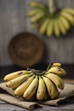 Taze sarı muzlar, ahşap masa üzerinde sade çuval bezi ile servis edilir.