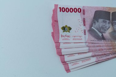 Bir yığın rupiah banknotları, Endonezya 100 bin rupia banknotları ve beyaz bir arka planı var.