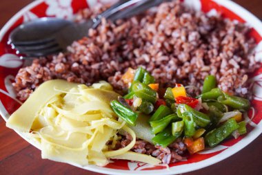 13 Şubat 2025 'te yakalanan kırmızı pirinç ve sebzeli Endonezya yemeği. Sağlıklı pirinç ve taze yeşilliklerin besleyici kombinasyonu sağlıklı ve lezzetli bir yemek oluşturur.