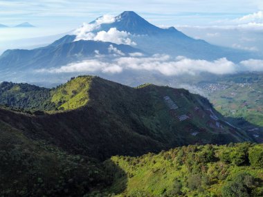 Endonezya 'nın merkezindeki Prau Dağı' nın havadan görüntüsü 28 Nisan 2025 'te çekildi. Yuvarlanan yeşil tepeler ve sisli tepeler berrak mavi gökyüzünün altında çarpıcı bir doğal manzara yaratır.