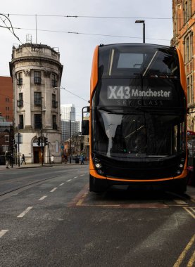 İki katlı İngiliz turuncu otobüsü durakta duruyor. Arka planda, sütunları olan eski yuvarlak bir taş bina var. Mimarisi farklı çağlardan kalma kentsel bir ortam..