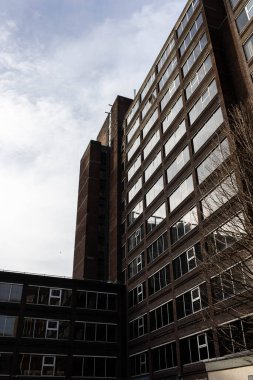 Birçok bölümden oluşan birçok penceresi olan yüksek tuğlalı modern bir bina. Ön planda yapraksız bir ağacın bir parçası görünür. Gökyüzü bulutlarla aydınlık.