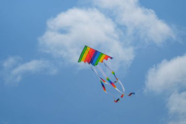 Mavi gökyüzü arka planındaki gökkuşağı gibi renkli kağıt uçurtmalar. Uçurtmalar sahil boyunca uçar. Havada güzel renkler. Doğal desen ve doku arkaplanı.